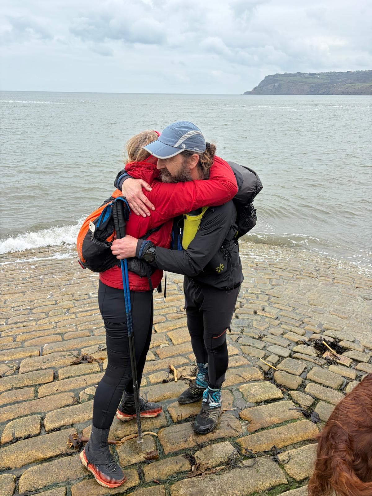 A runner embracing a friend at the Robin Hood&rsquo;s Bay coast finish after completing a Community Traverse ultra