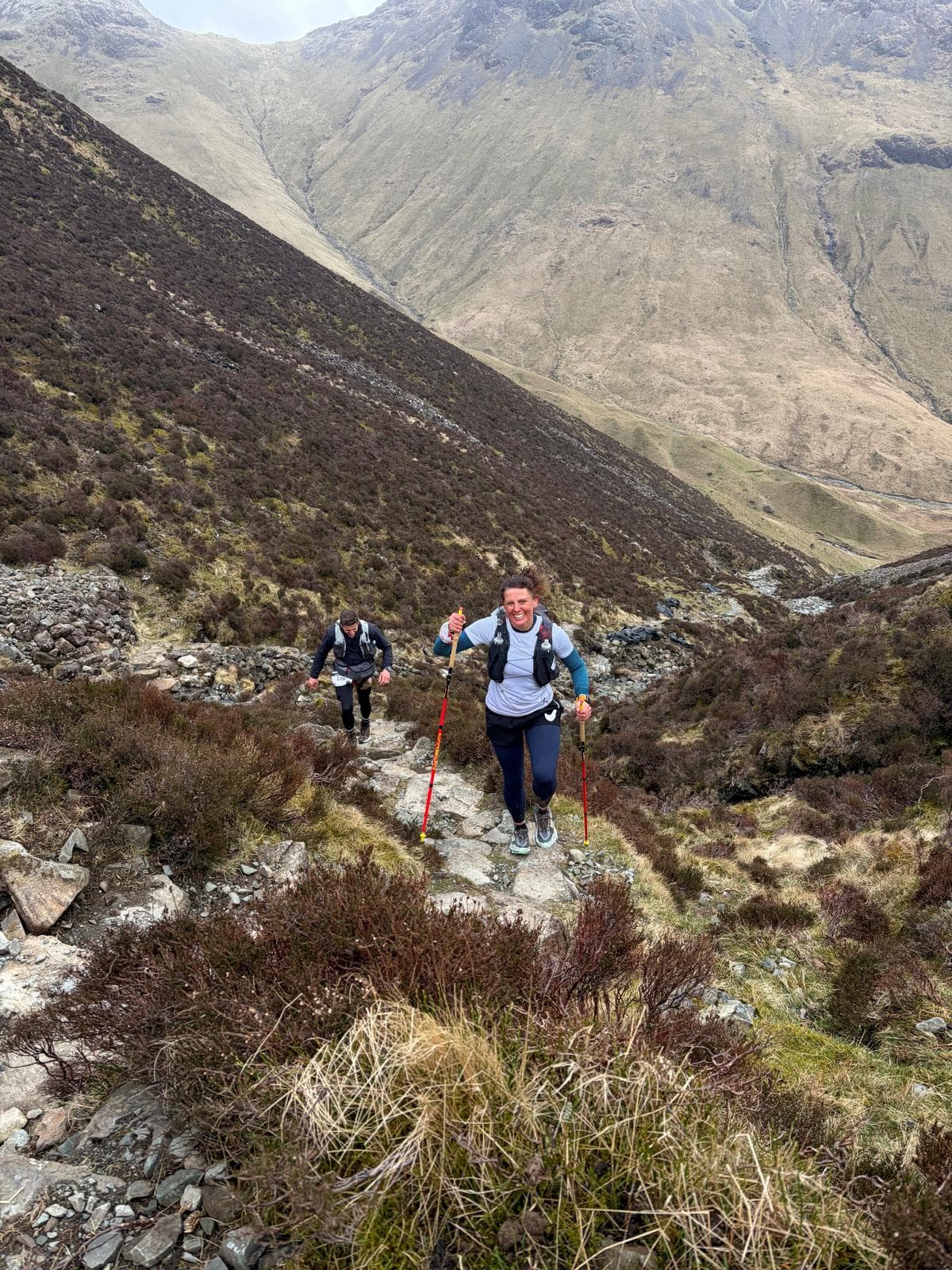 Two ultra runners with poles ascending a steep mountain path in the Lake District