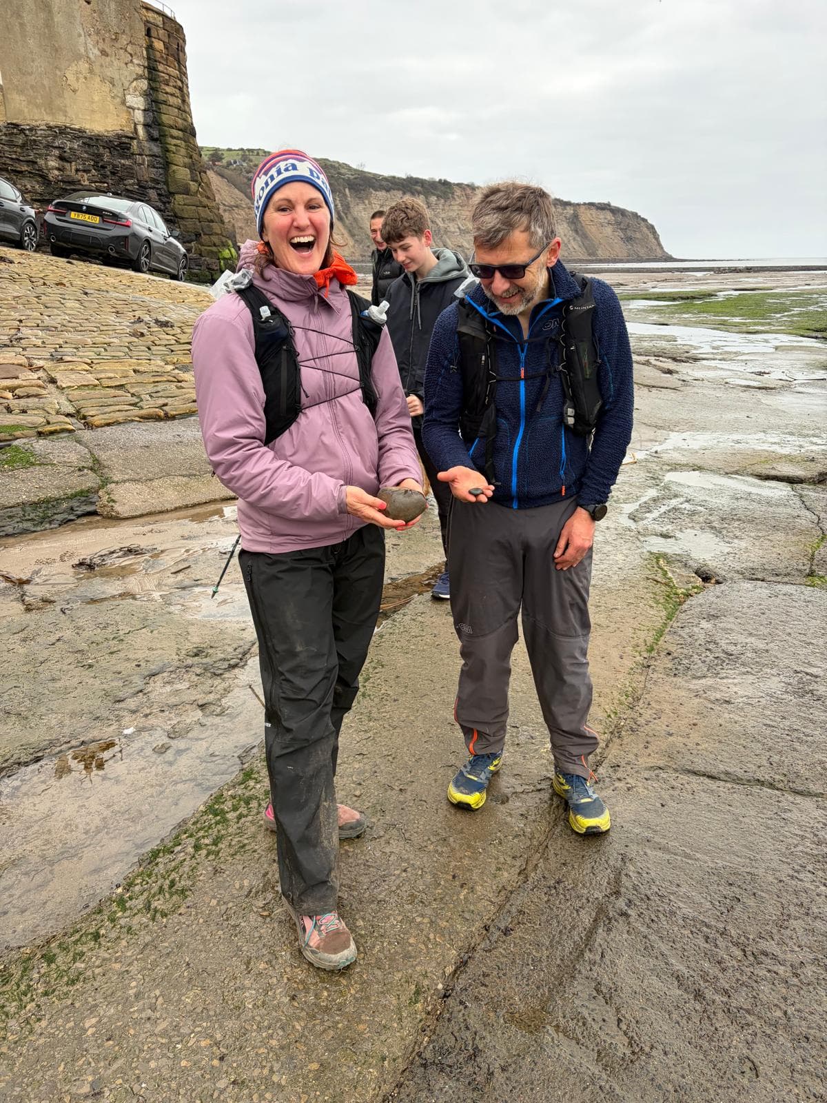 Two Community Traverse runners laughing together on the rocky shore at the coast
