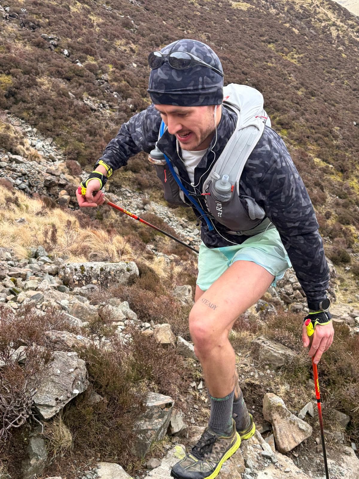 Solo trail runner with poles climbing rough heather and rocky fell terrain