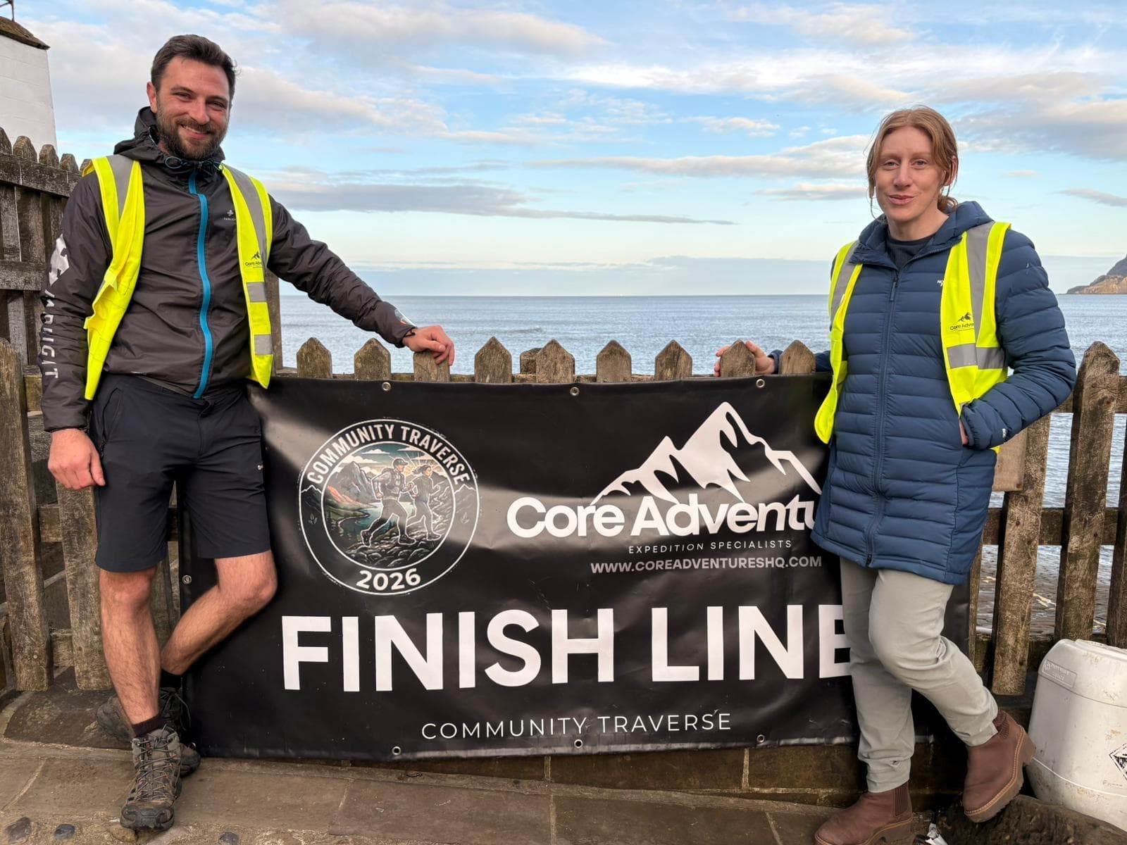 Community Traverse volunteers at the Robin Hood&rsquo;s Bay finish line banner on a sunny day at the coast
